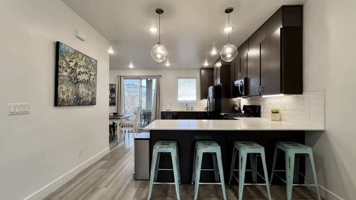 A modern kitchen with a central island, bar stools, pendant lighting, and dark cabinetry.