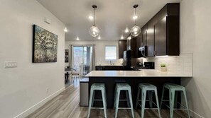 A modern kitchen with a central island, bar stools, pendant lighting, and dark cabinetry.