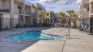 A modern hotel with a swimming pool, outdoor seating, and a clear sky.