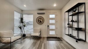 A modern living room with a sofa, a chair, a potted plant, a wall-mounted shelf, and a door with glass panels. - The Lofts #44 | Townhome Pool Resort (Saint George)