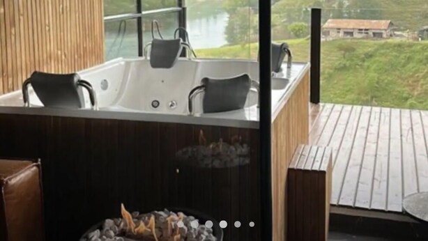 A modern bathroom with a large bathtub, a fireplace, and a view of a lake and hills. - Apartment with lake access and jacuzzi in El Peñol, Antioquia (Peñol)
