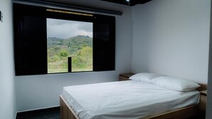 A bedroom with a bed, a nightstand, and a window with a view of a hilly landscape. - Apartment with lake access and jacuzzi in El Peñol, Antioquia (Peñol)
