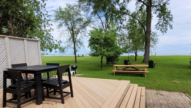 A wooden deck with a table and chairs, a picnic table, and a grill area. - Waterfront Cottage with a sand beach! (Green Bay)