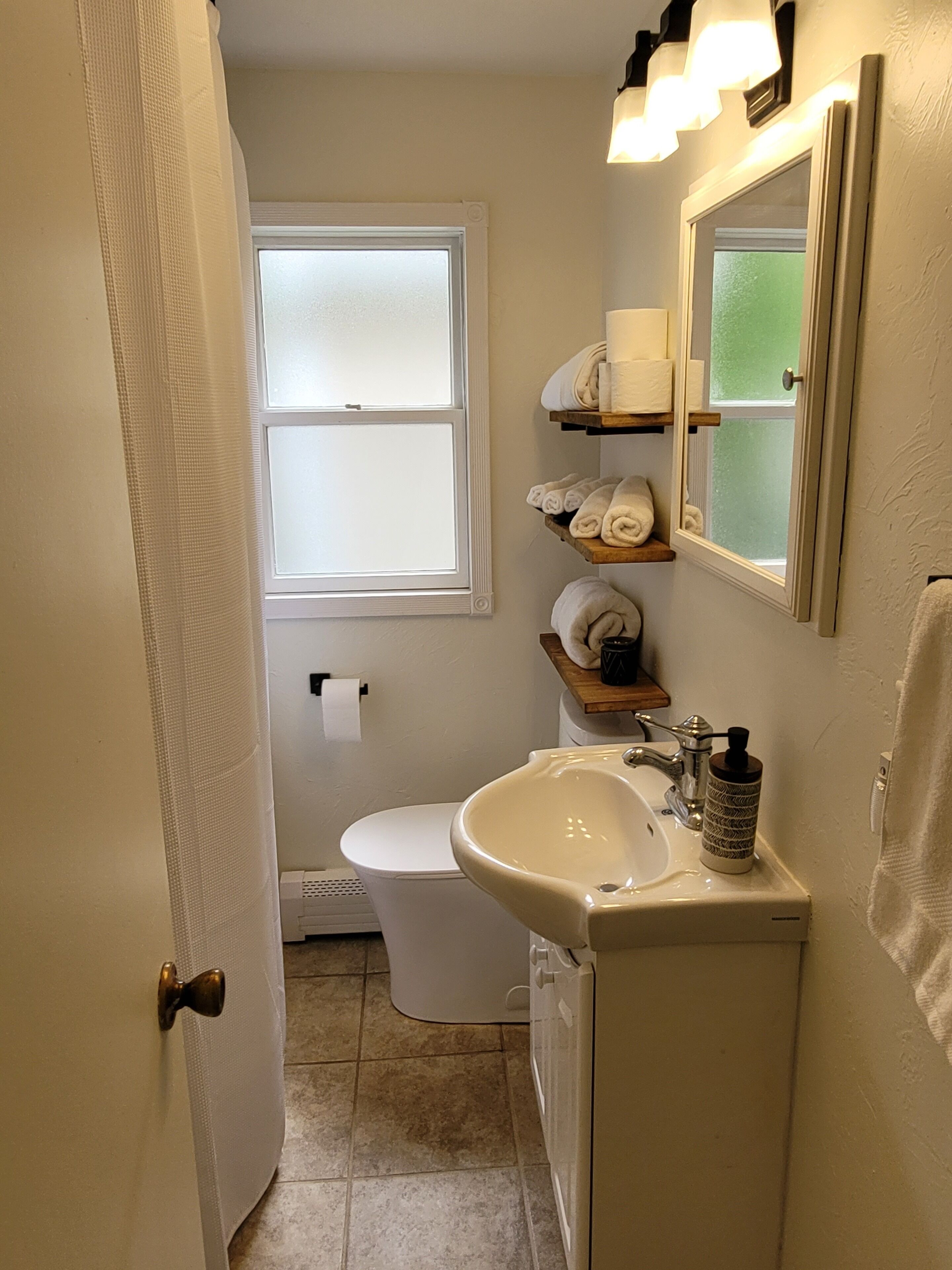 A compact bathroom with a toilet, sink, and towel storage.