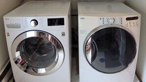 Two front-loading washing machines with shelves above containing folded towels and linens. - Waterfront Cottage with a sand beach! (Green Bay)