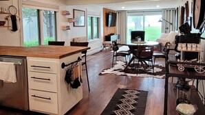 A modern kitchen with a wooden countertop, white cabinetry, and a dining area with a table and chairs. - Waterfront Cottage with a sand beach! (Green Bay)