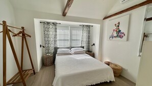 A bedroom with a bed, wooden floor, window with curtains, and a wall-mounted air conditioner.