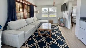 A modern living room with a sofa, a patterned rug, a ceiling fan, and a TV.