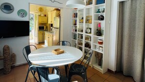Ein Essbereich mit einem runden Tisch, schwarzen Stühlen, einer weißen Pendelleuchte und einer Küche im Hintergrund.