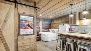 A rustic interior with a bed, a kitchen area, and a bar with stools. - Casas Coastal Experience Cabin A (Rockport)