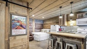 A rustic kitchen with wooden cabinets, a white refrigerator, and a bar area with stools. - Casas Coastal Experience Cabin A (Rockport)