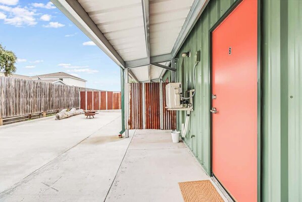 Un espacio exterior cubierto con una puerta roja, una valla de madera y un suelo de hormigón.