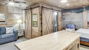 Une pièce avec un plafond en bois, un canapé bleu, une table en bois et un lit recouvert d’une courtepointe blanche.