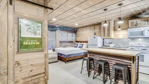 Une cuisine compacte dotée d’un îlot central, de tabourets de bar et d’un lit avec une tête de lit bleue.