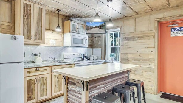 Une cuisine avec des meubles en bois, un four à micro-ondes, un évier et un grand îlot central doté de tabourets.