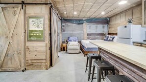 Une pièce compacte comprenant un lit, un petit coin salon, une kitchenette et une porte en bois ornée d’une affiche.