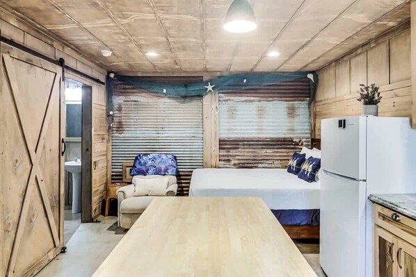 A compact room with a wooden table, two beds, a refrigerator, and a sink.
