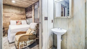 Ein Schlafzimmer mit Holzwänden, einem Bett, einem Korbsessel und einem Badezimmer mit Waschbecken und Spiegel.