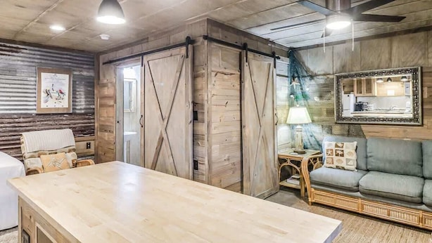 Ein Zimmer mit Holztisch, einer Couch, einem Deckenventilator und einem gerahmten Bild an der Wand.