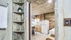 Eine kompakte Küche mit Holzschränken, einem weißen Kühlschrank und einem Essbereich mit einem Korbstuhl.