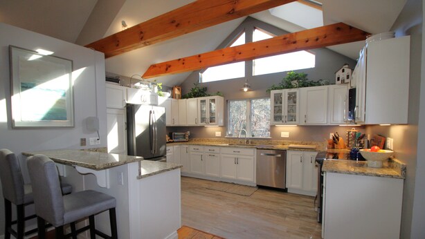 A modern kitchen with white cabinetry, a central island with bar stools, and wooden beams on the ceiling. - Updated 3 Bedroom Offering Hot Tub and Large Yard (2360) (Brewster)