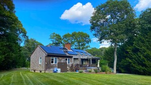 A house with solar panels on the roof, a covered porch, and a lawn. - Updated 3 Bedroom Offering Hot Tub and Large Yard (2360) (Brewster)