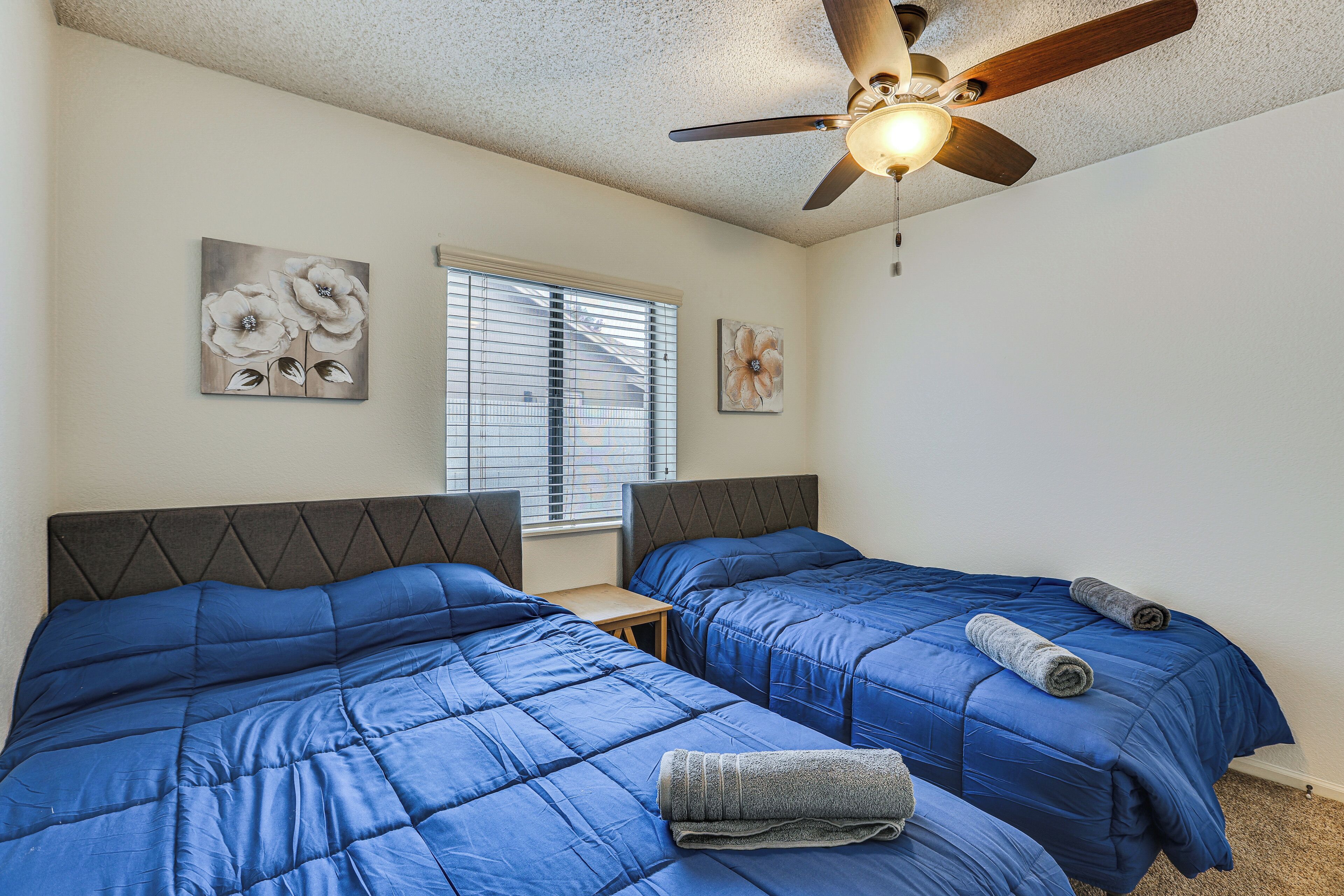 A bedroom with two beds, a ceiling fan, and artwork on the walls.