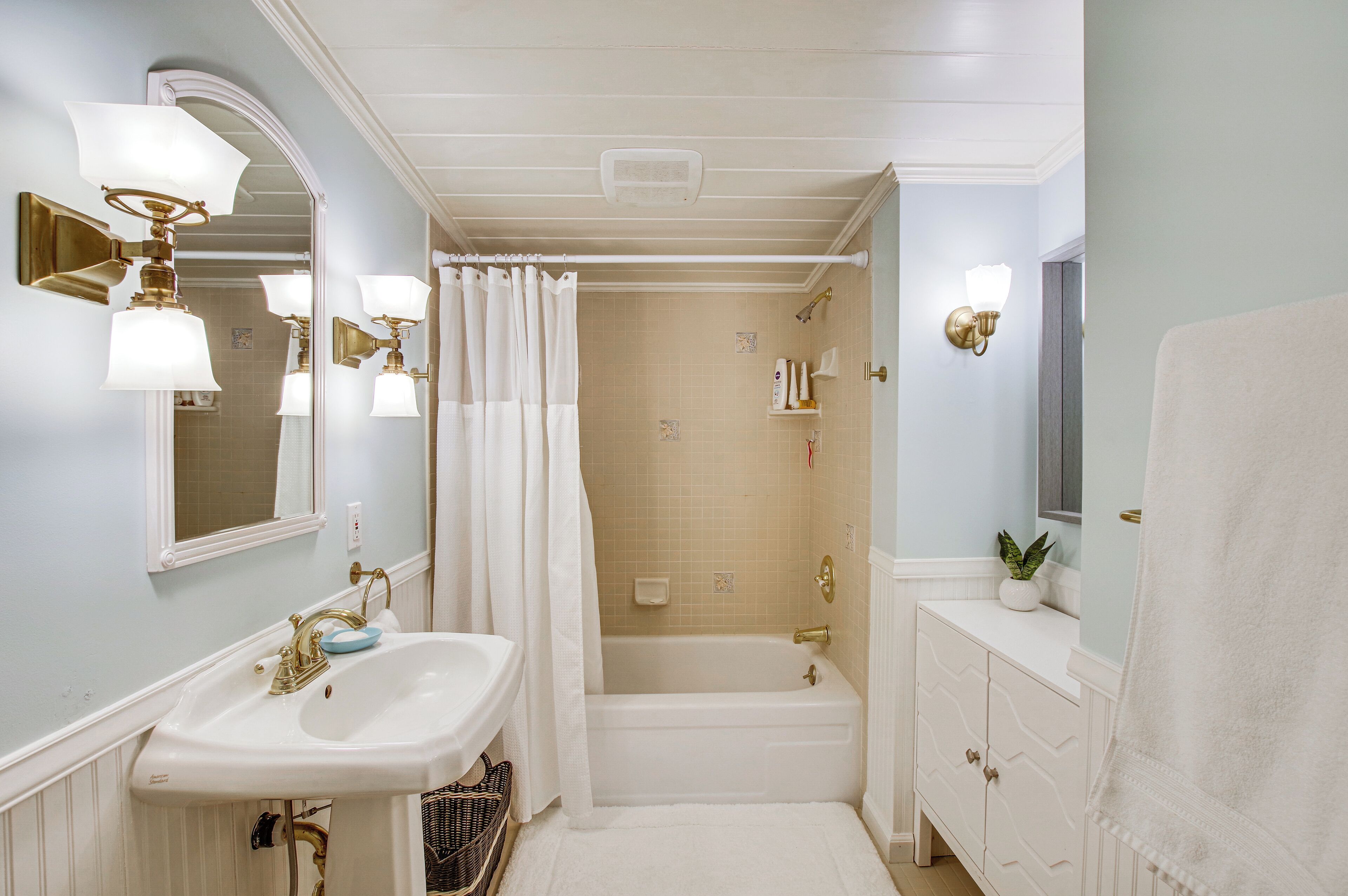 Une salle de bain avec un lavabo blanc, des robinetteries dorées, une baignoire et une serviette blanche.