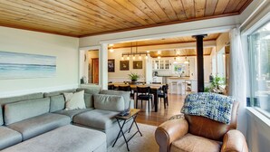 A modern living room with a sectional sofa, a leather armchair, and a dining area with a wooden table and chairs. - Puget Sound Cottage w/ Private Community Beach! (Coupeville)