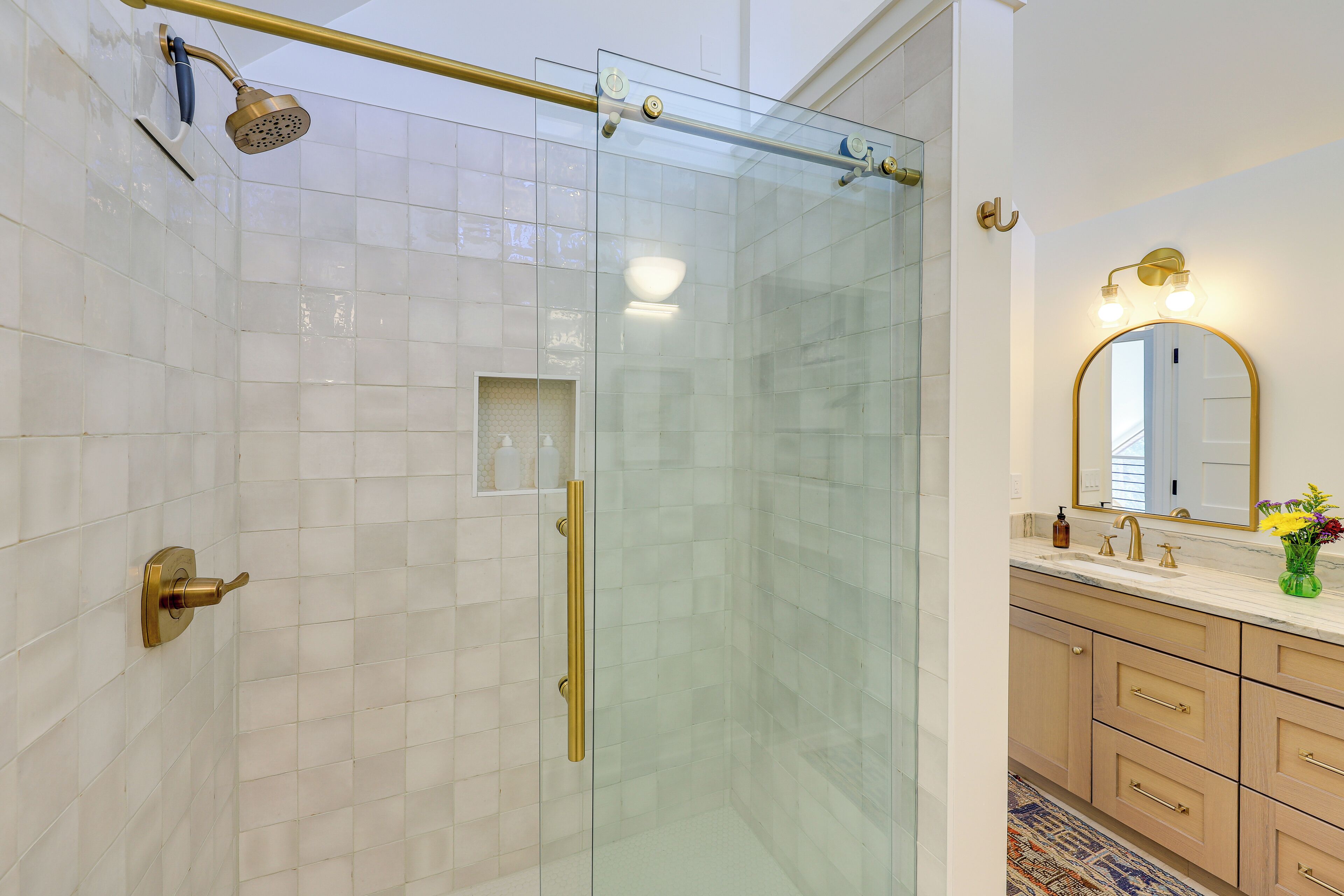 A modern bathroom with a glass-enclosed shower, a vanity with a mirror, and a patterned rug.