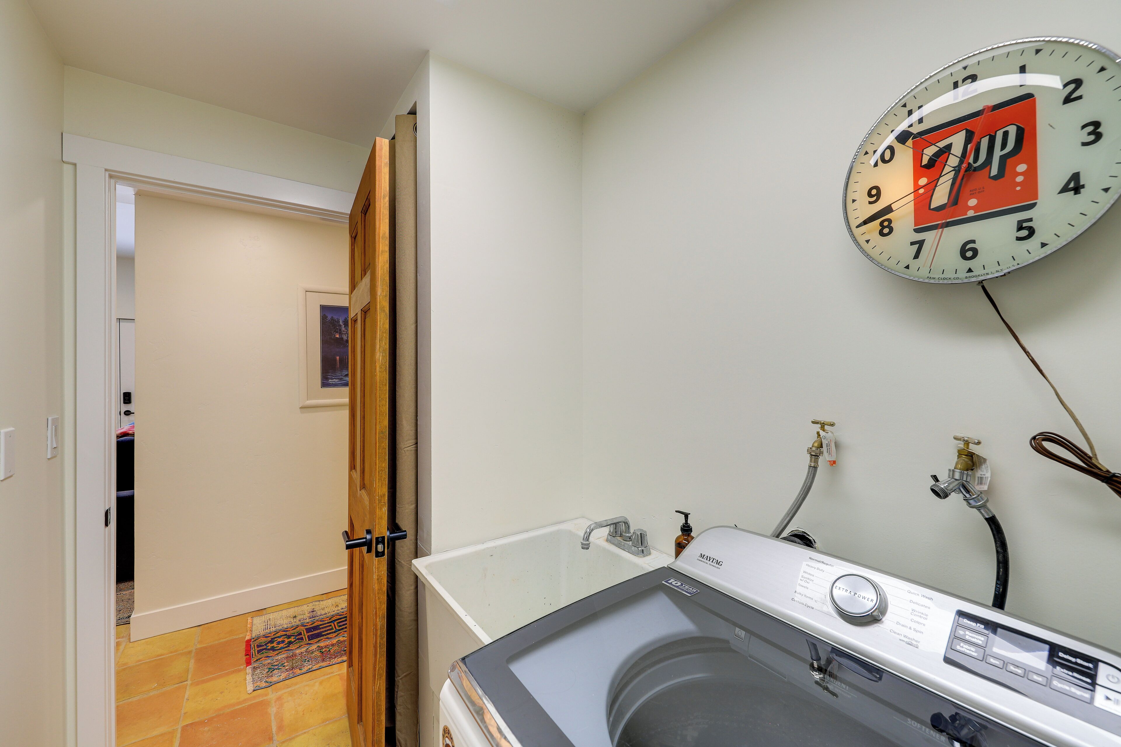 A laundry room with a washing machine, a sink, and a 7UP clock on the wall.