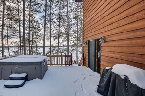 Puuinen mökki, jossa on terassi, poreallas ja katettu esine.
