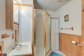 Un bagno con un mobile vanitario in legno, un lavandino, uno specchio, una doccia con porta in vetro e un porta asciugamani.