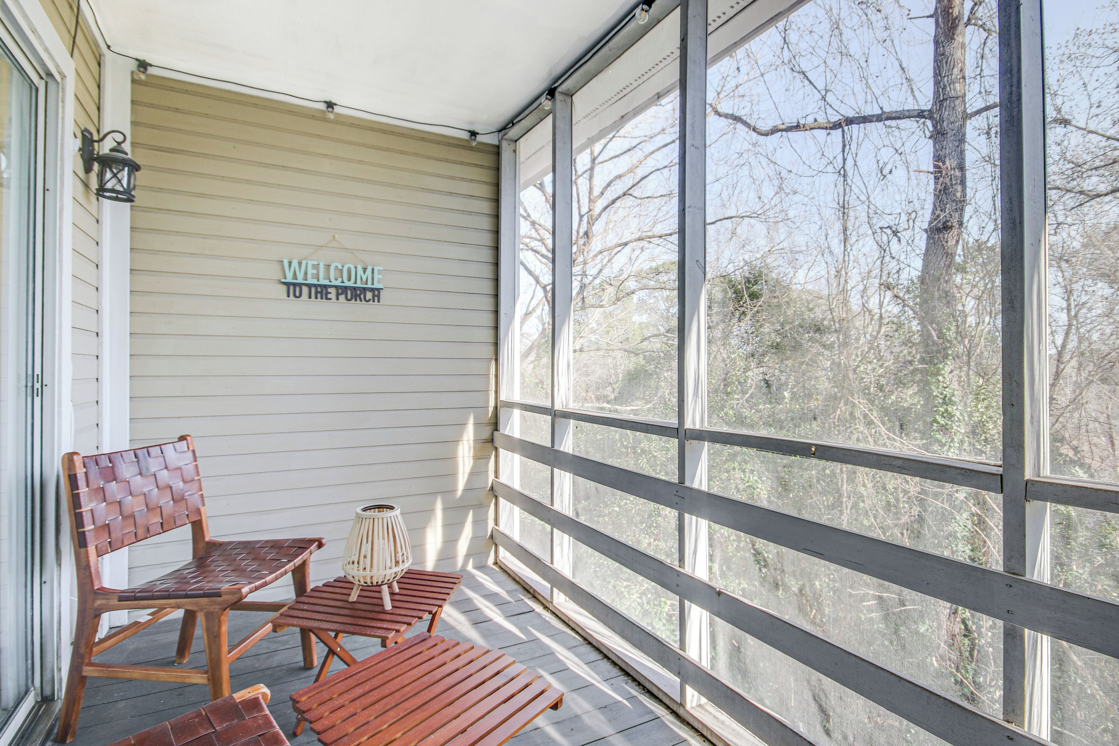 A covered porch with a 'WELCOME TO THE PORCH' sign, wooden furniture, and a view of trees through large windows.