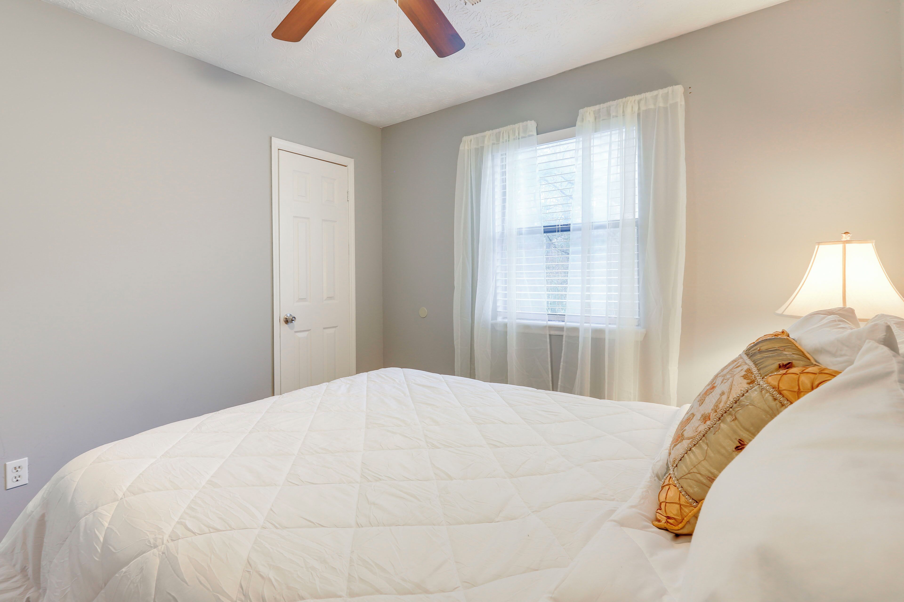 A bedroom with a bed, a door, a window with curtains, and a lamp.
