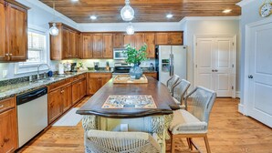 A spacious kitchen with wooden cabinets, a central island, and a dining area with wicker chairs. - Lakefront Jacksons Gap Retreat w/ Grill & Dock! (Jacksons' Gap)