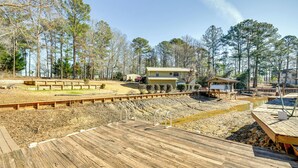 A wooden deck with a metal railing, a small pond, and a house in the background. - Lakefront Jacksons Gap Retreat w/ Grill & Dock! (Jacksons' Gap)
