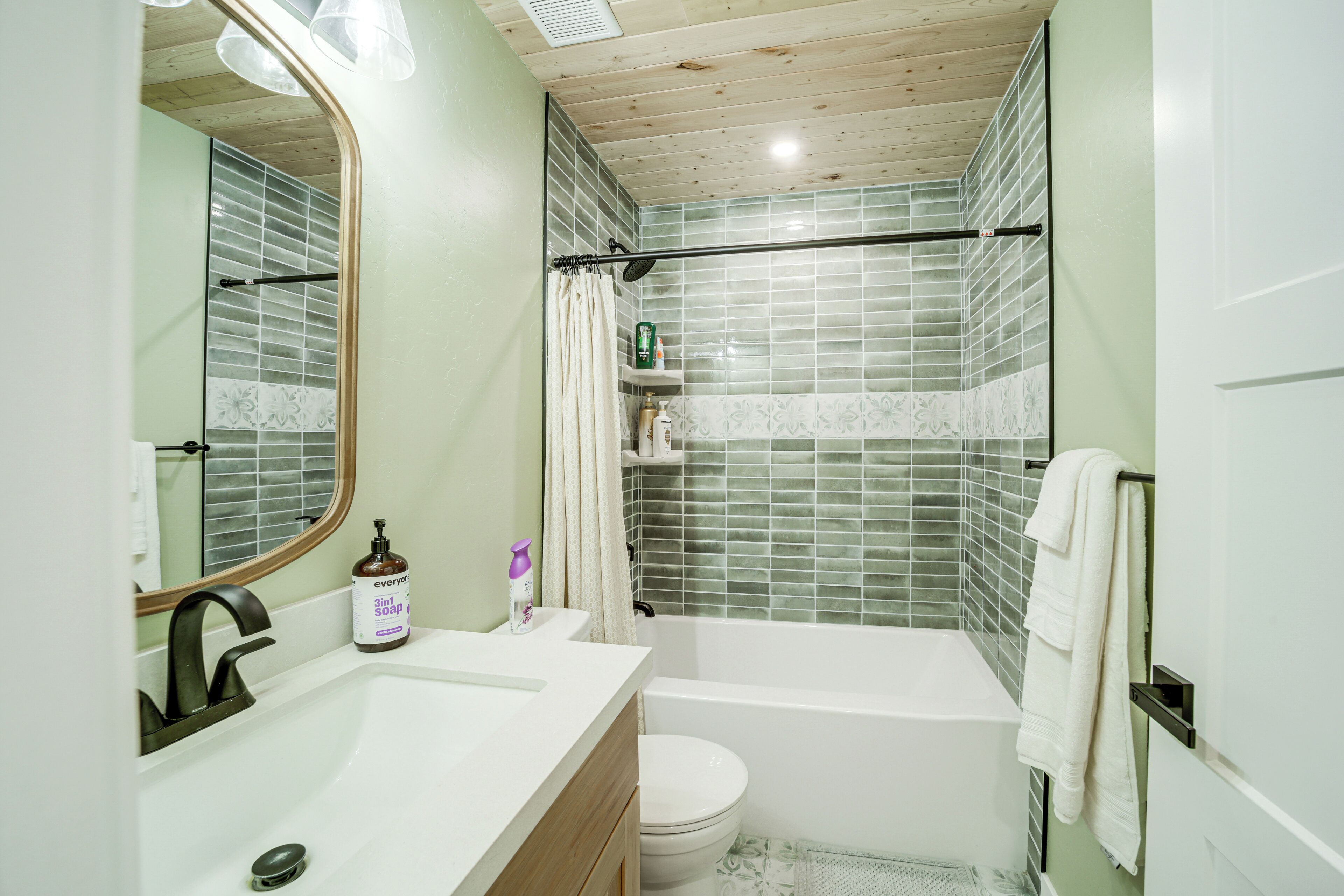 A bathroom with a wooden ceiling, a white sink, a bathtub, and a shower curtain.