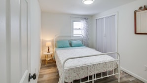 A bedroom with a white metal bed frame, a floral bedspread, and a window with curtains. - Riverfront Topsham Home ~ 28 Mi to Portland! (Topsham)