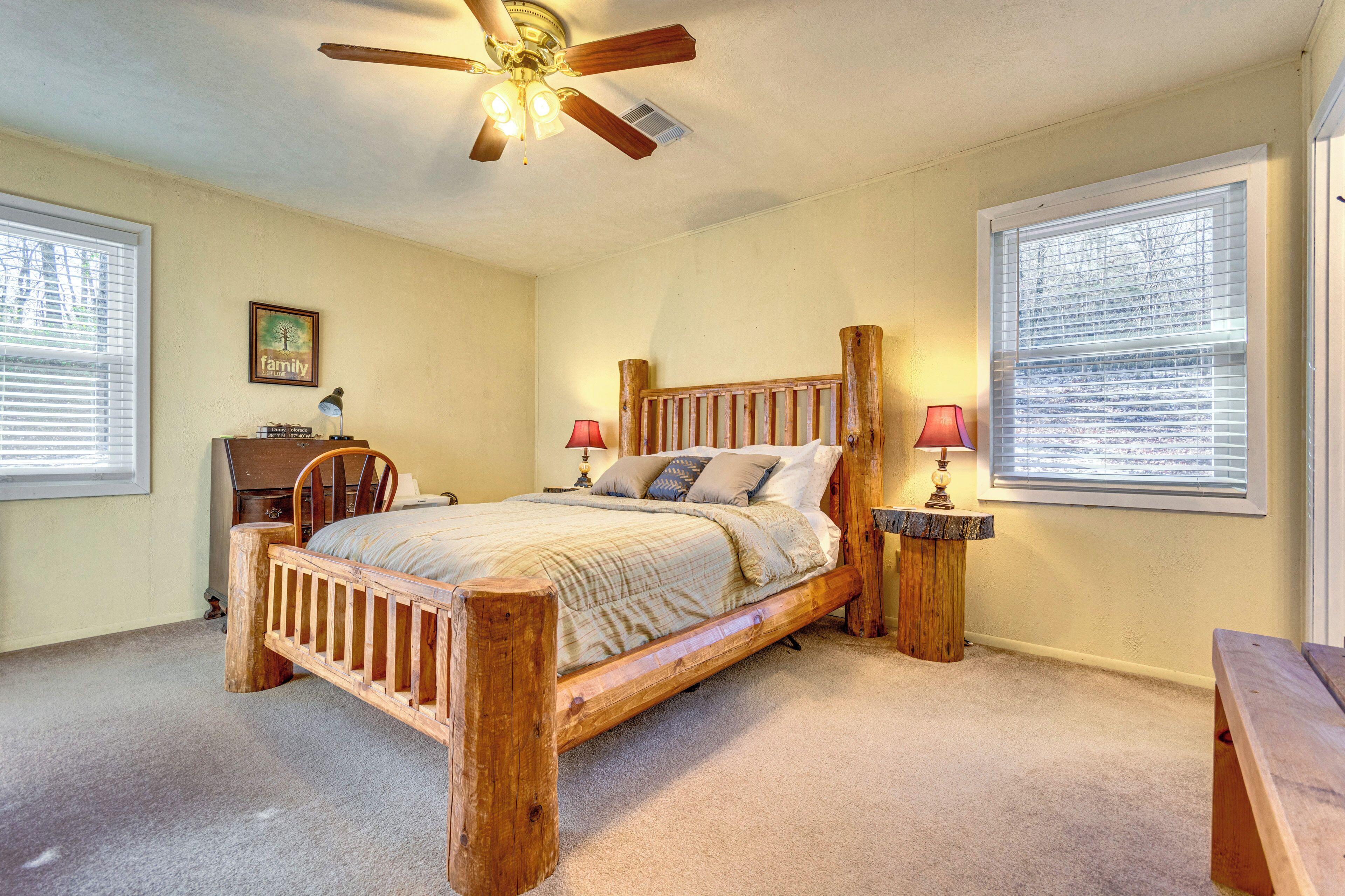 A bedroom with a wooden bed, two bedside tables with lamps, a ceiling fan, and a window with blinds.