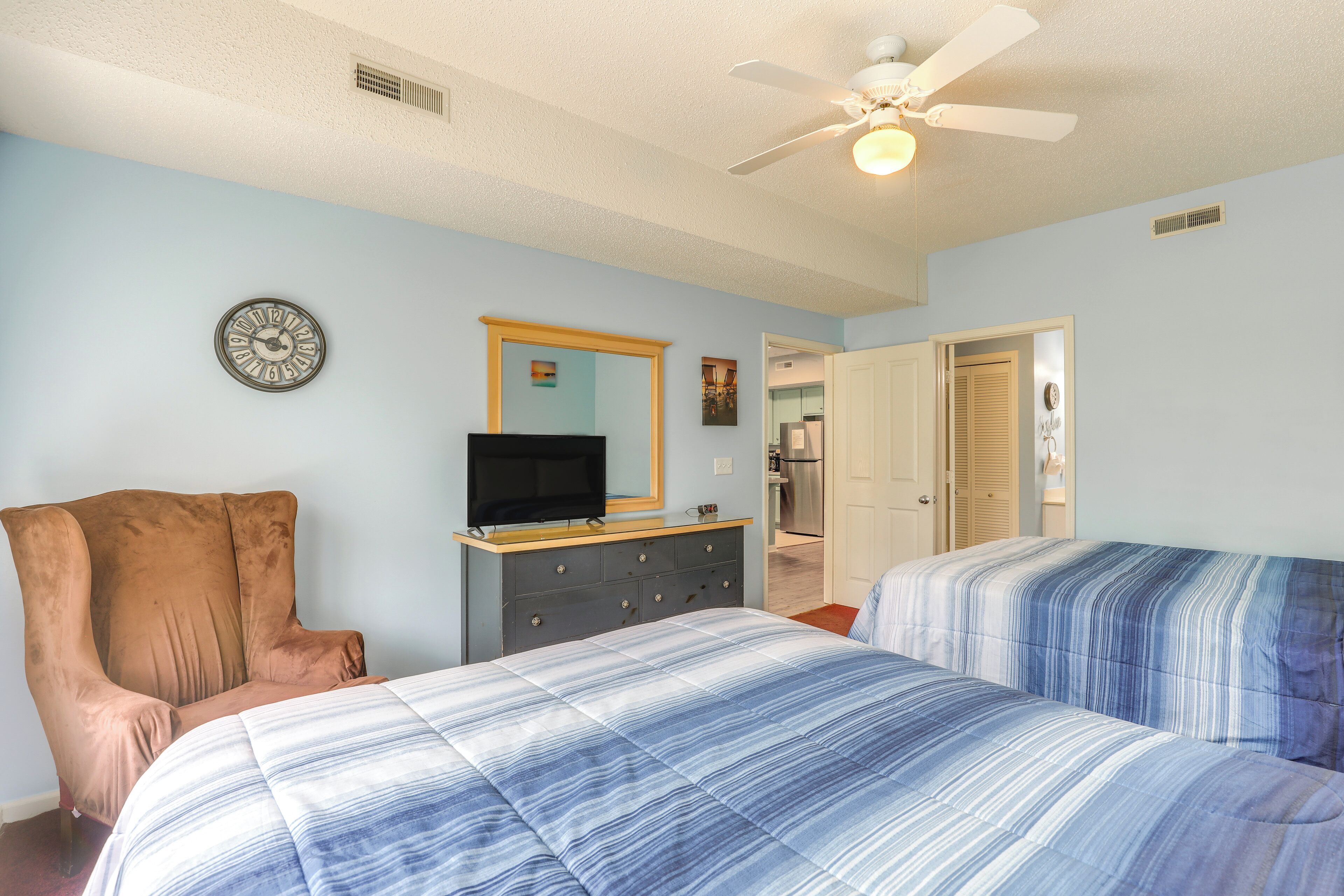 A bedroom with two beds, a TV on a dresser, a clock on the wall, and a ceiling fan.