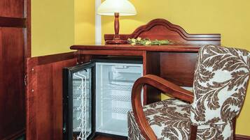 Un frigorifero compatto con porta in vetro, una sedia in legno con cuscino decorato, e un tavolino con lampada e fiori.