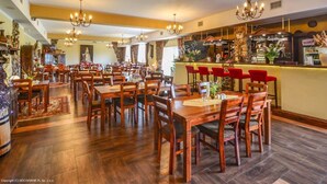 Un restaurante espacioso con varias mesas y sillas de madera, una zona de bar e iluminación decorativa.