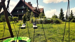 Un espacio al aire libre con césped, dos asientos para columpios y una estructura de madera.