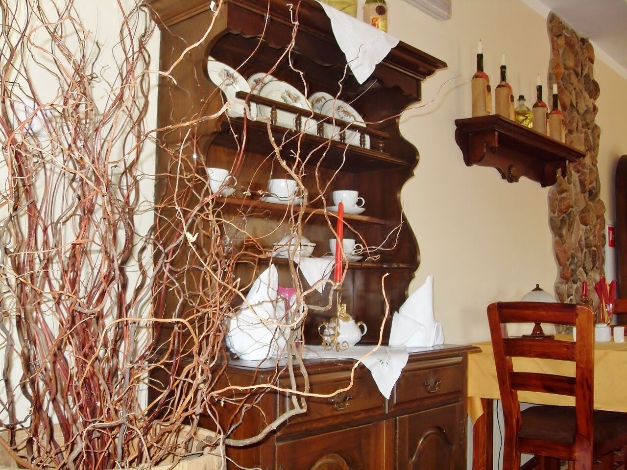 Un área de comedor con un armario de madera, una mesa con una silla y una pared decorativa con botellas y un detalle de piedra.