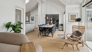 A spacious living area with a dining table set for six, a large plant, and a wicker chair with a fur throw. - Nice home in Otterup with sauna (Otterup)