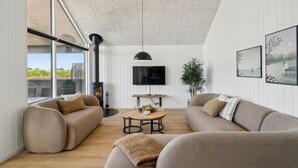 A modern living room with a fireplace, a television, and a large window overlooking a garden. - Nice home in Otterup with sauna (Otterup)