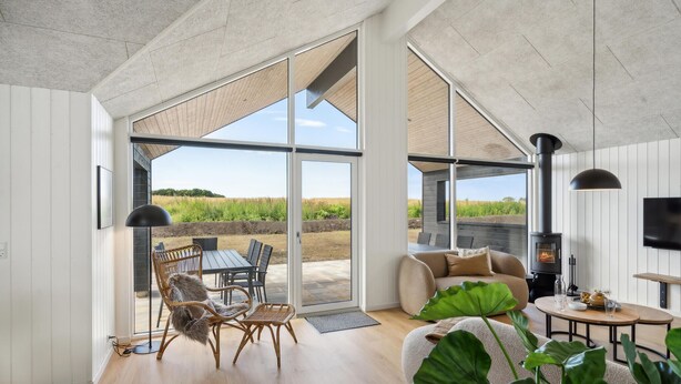 A spacious living room with a large sliding glass door leading to an outdoor area, a cozy seating area with a sofa and chairs, a fireplace, and a television mounted on the wall. - Nice home in Otterup with sauna (Otterup)