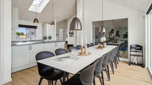 A modern kitchen with a large island, pendant lighting, and a dining area with a long table and chairs. - Nice home in Otterup with sauna (Otterup)