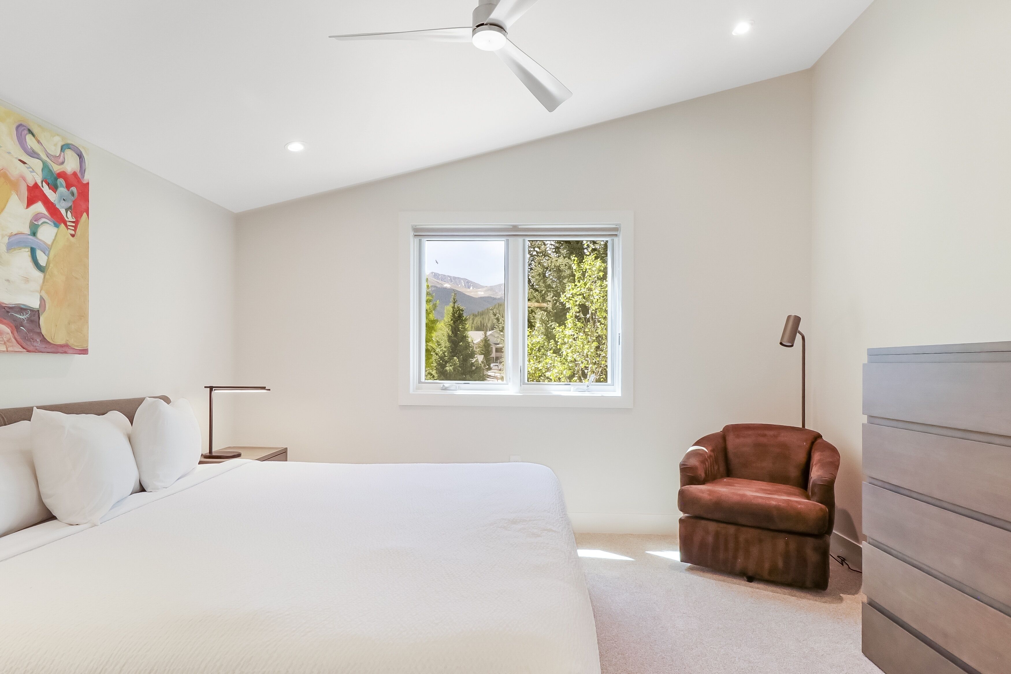 A bedroom with a bed, a chair, a dresser, a window, and a ceiling fan.